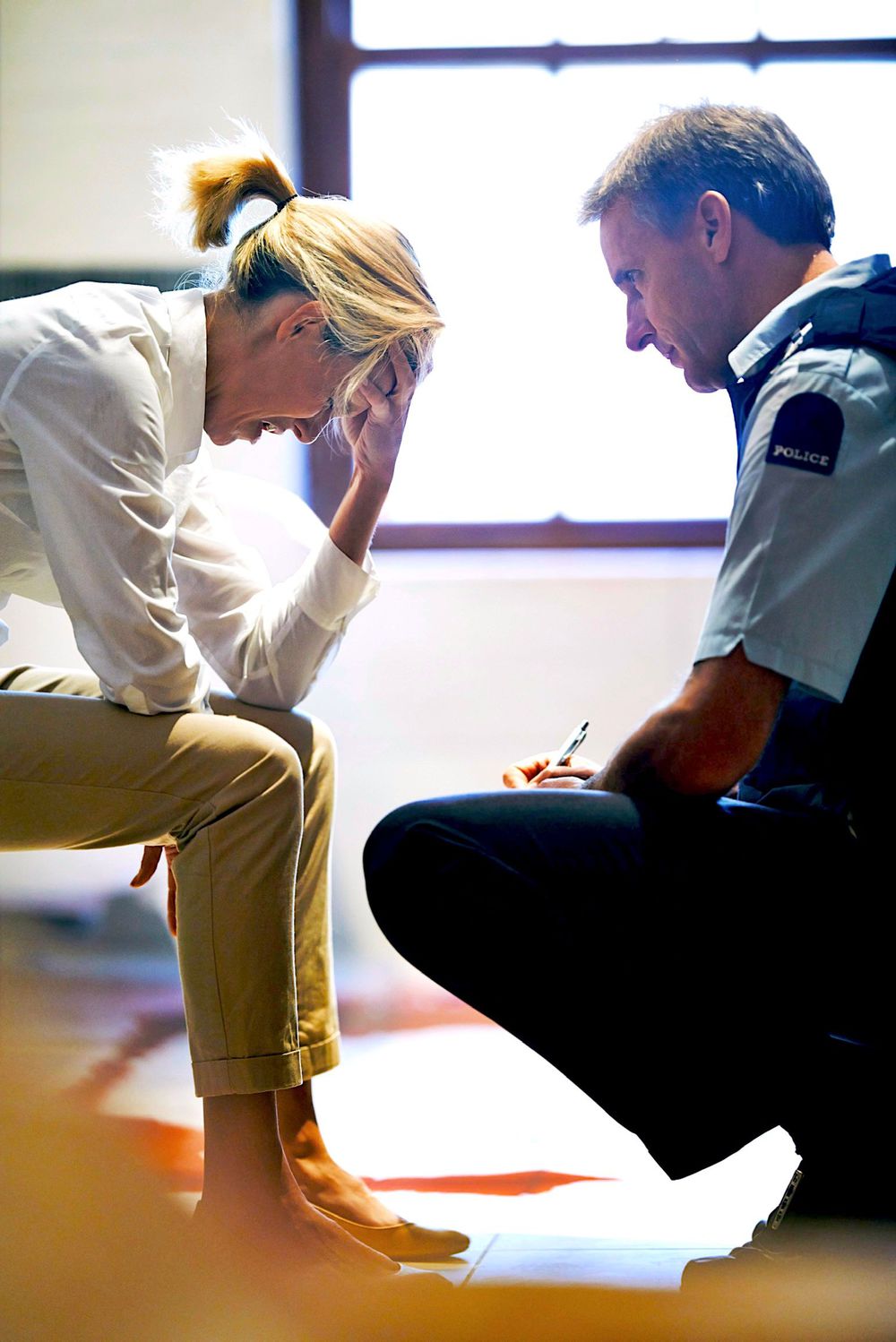 A police officer kneeling beside a distressed woman, taking notes